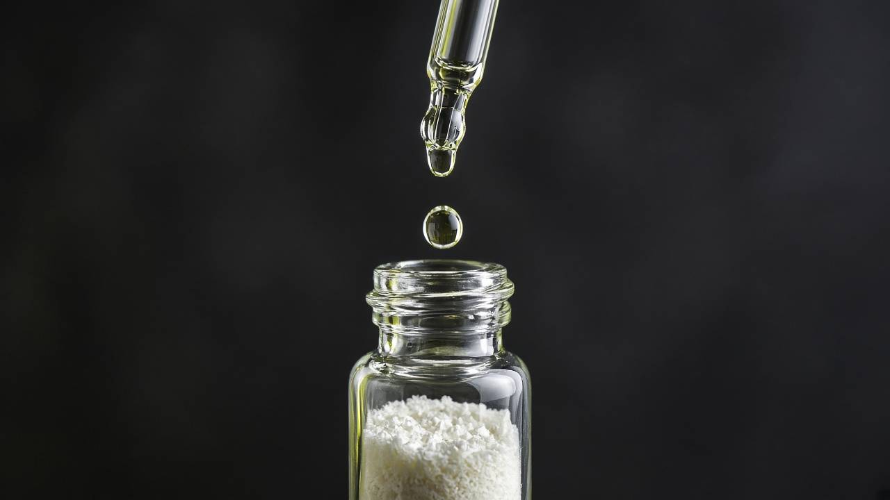 A drop of clear liquid falling from a glass dropper into an open vial of white powder